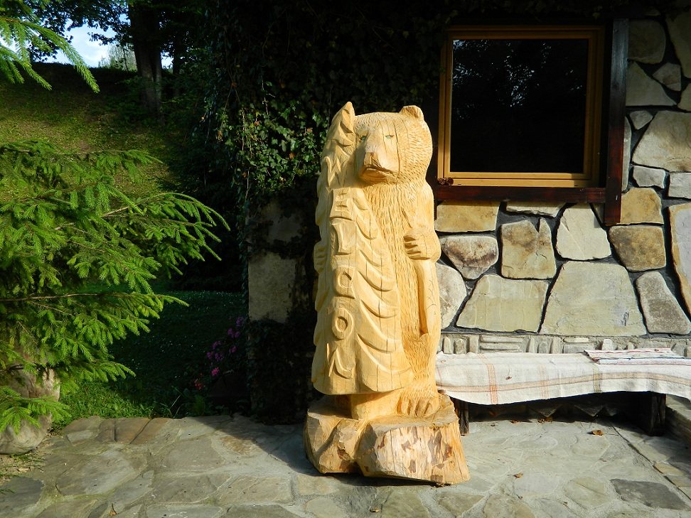 Urs sculptat în lemn, lângă o casă
